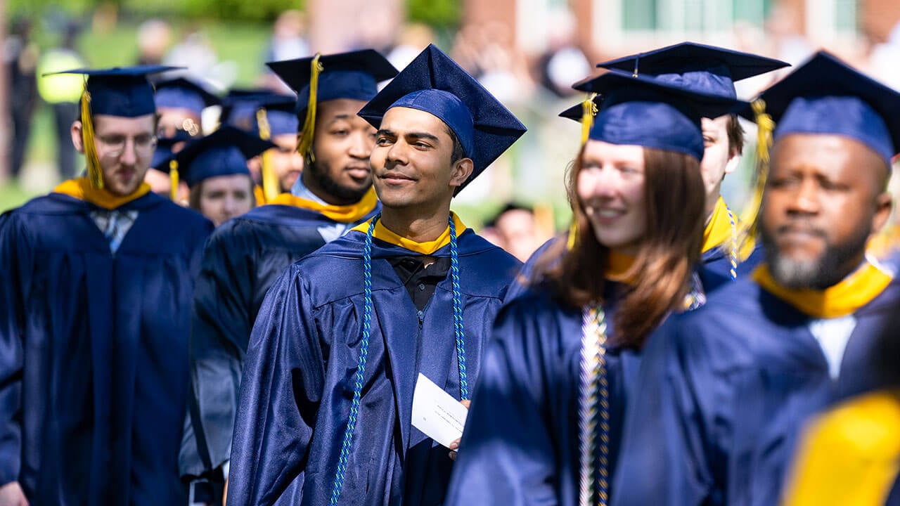 A graduate in the procession line smiling into the distance