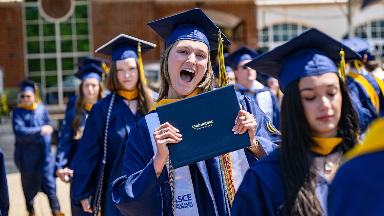 A graduate cheering while holding their diploma