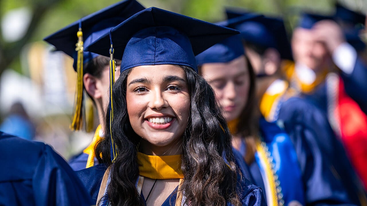 A graduate with long brown hair smiles