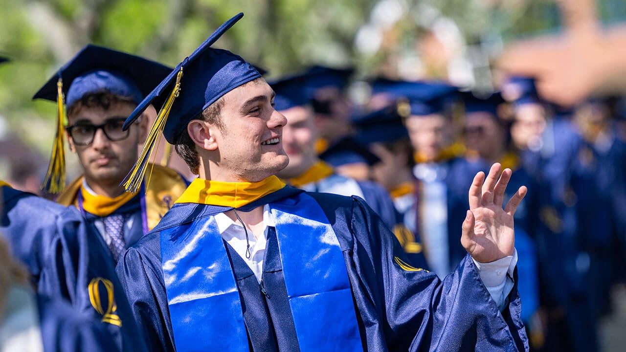 A graduate in the procession line waves into the distance
