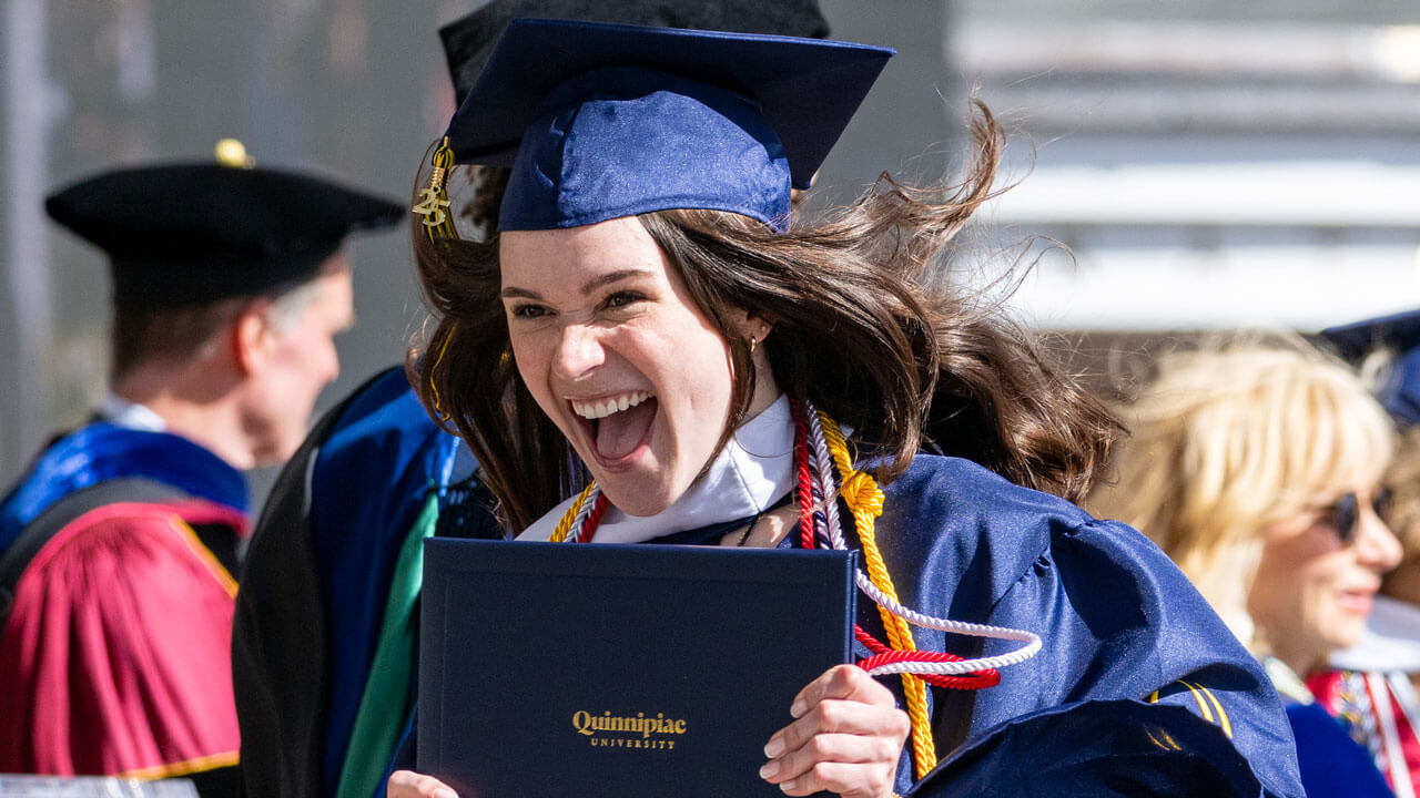 Graduate smiles with their diploma as they walk off the commencement stage.