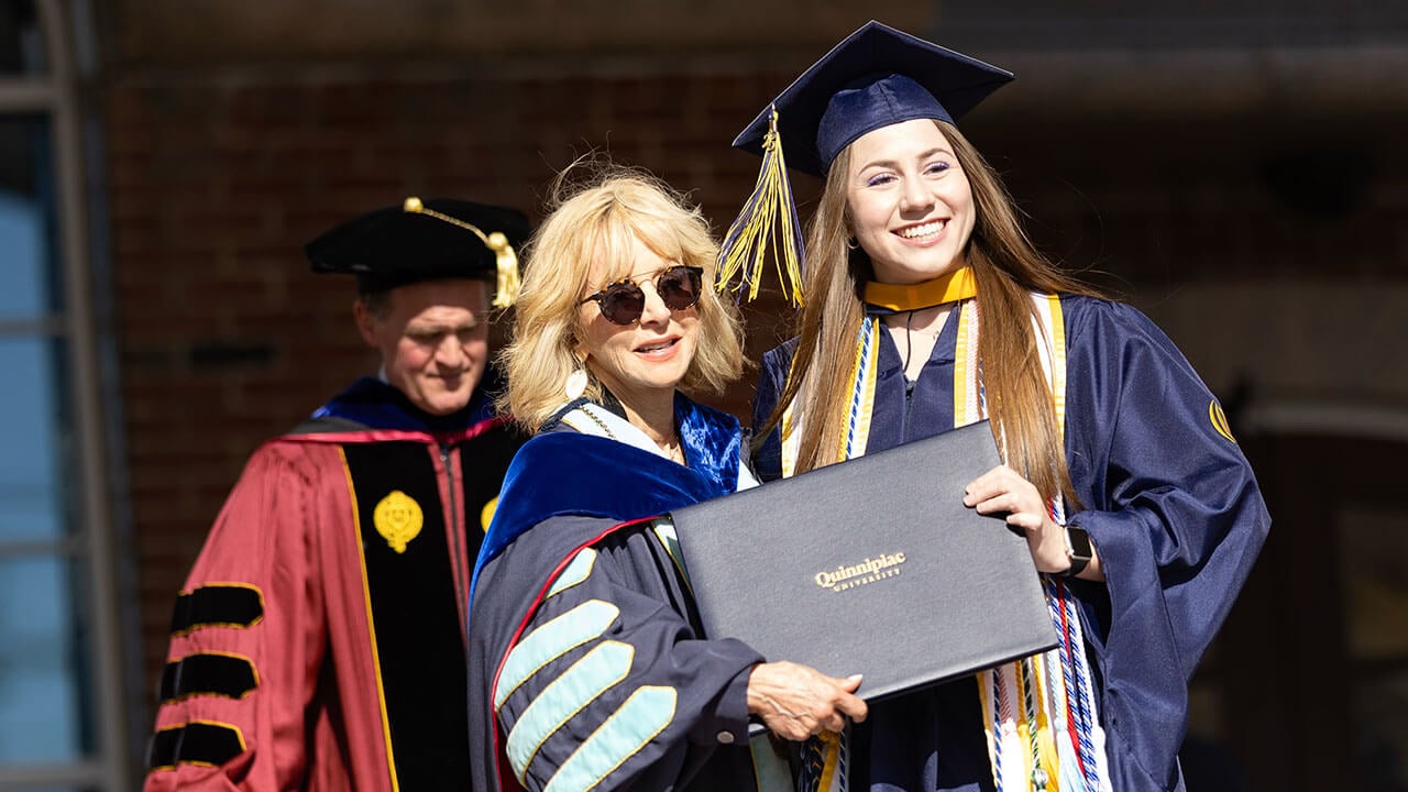 Madison Vale posing with her diploma next to President Judy Olian