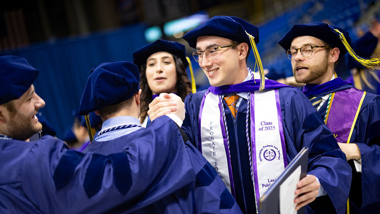 Two graduates shake hands and smile after getting their diplomas