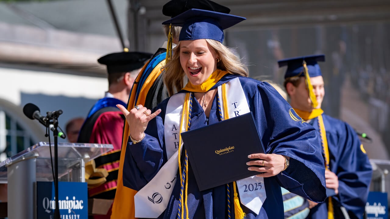 A grad sticking their tongue out excitedly with their diploma