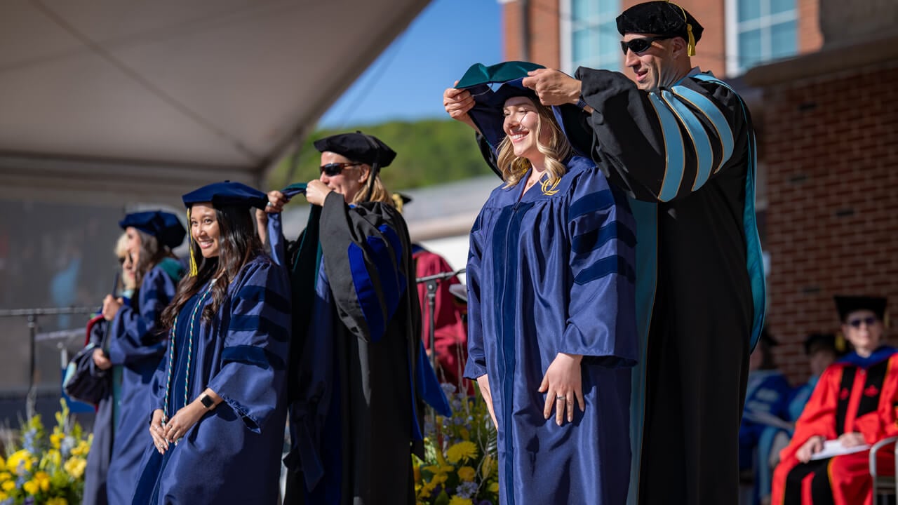 Graduates receive their doctoral hoods on the commencement stage.