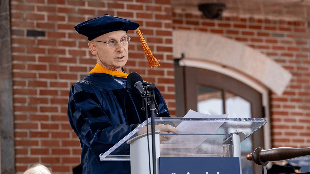 Dean Larry Slater speaking at podium wearing commencement regalia.