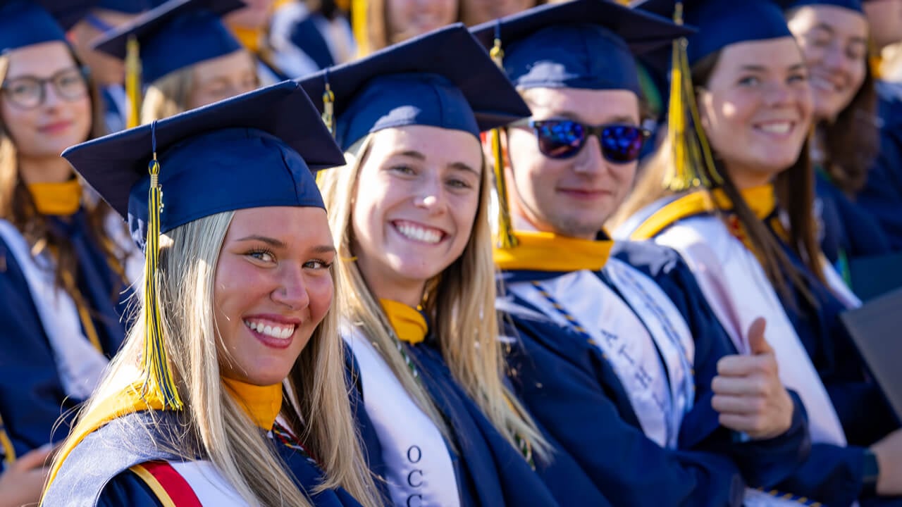 Graduates smile from their seats in the crowd.
