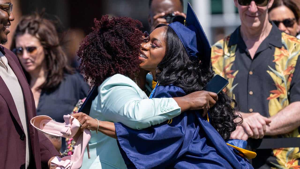 Graduate hugs their loved one with their shoes in their hand.