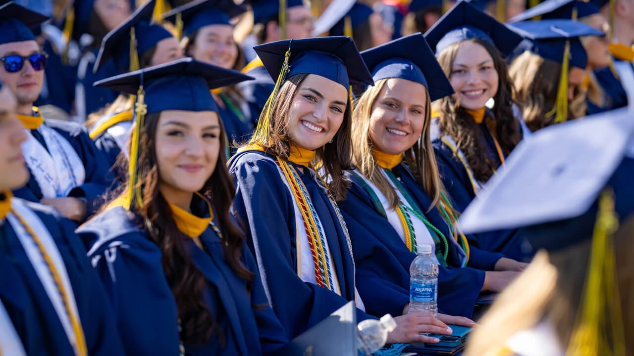 Graduates smile from their seats in the crowd.
