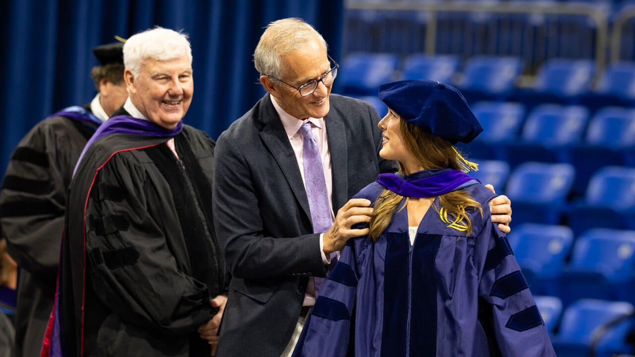 Graduate smiles at faculty member after receiving her hood.
