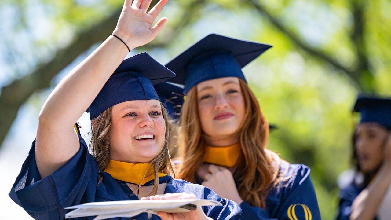 A graduate raises their hand and smiles