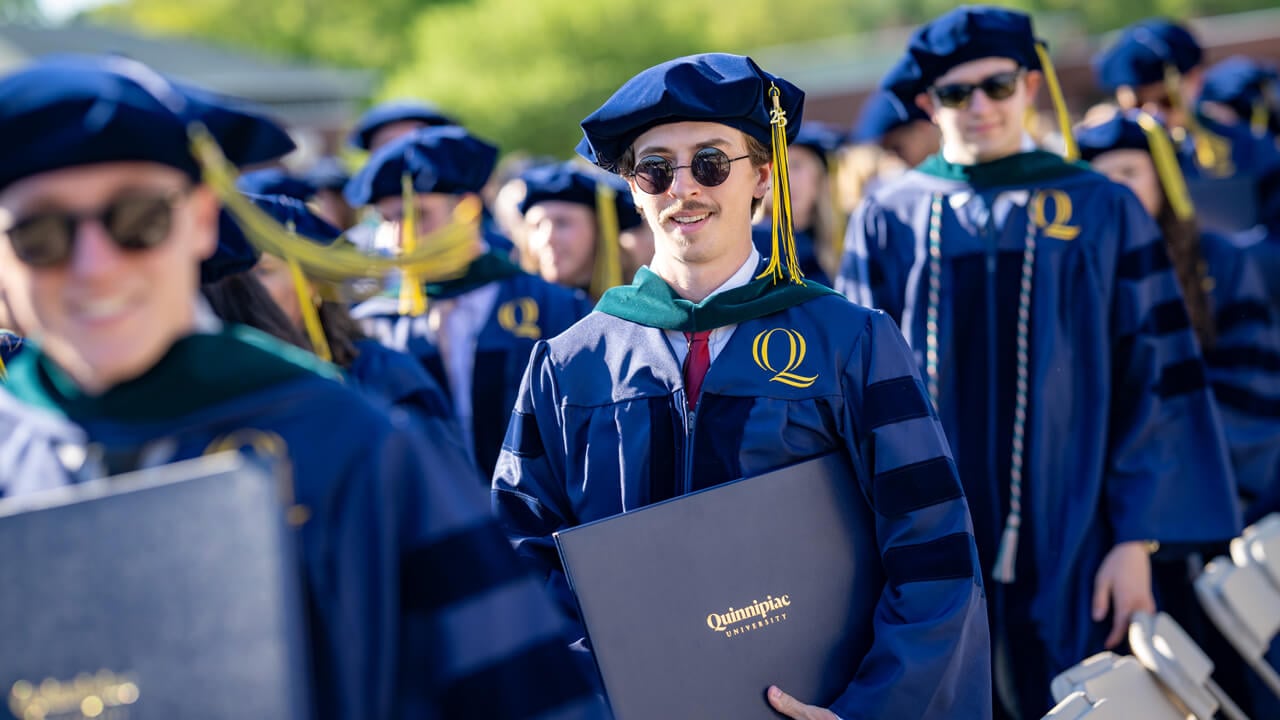 Graduates hold their diplomas and walk in a line