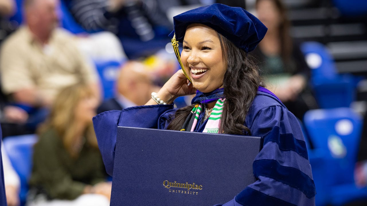 Graduate smiles and walks with diploma.