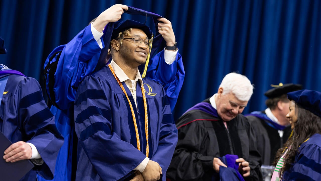 Graduate smiles while receiving his hood.