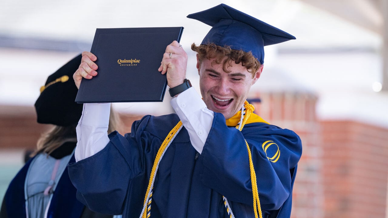 Graduate cheers, holding their diploma high, as they exit the commencement stage.