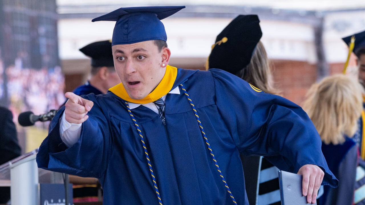 Graduate points in excitement as they exit the commencement stage, their diploma in hand.