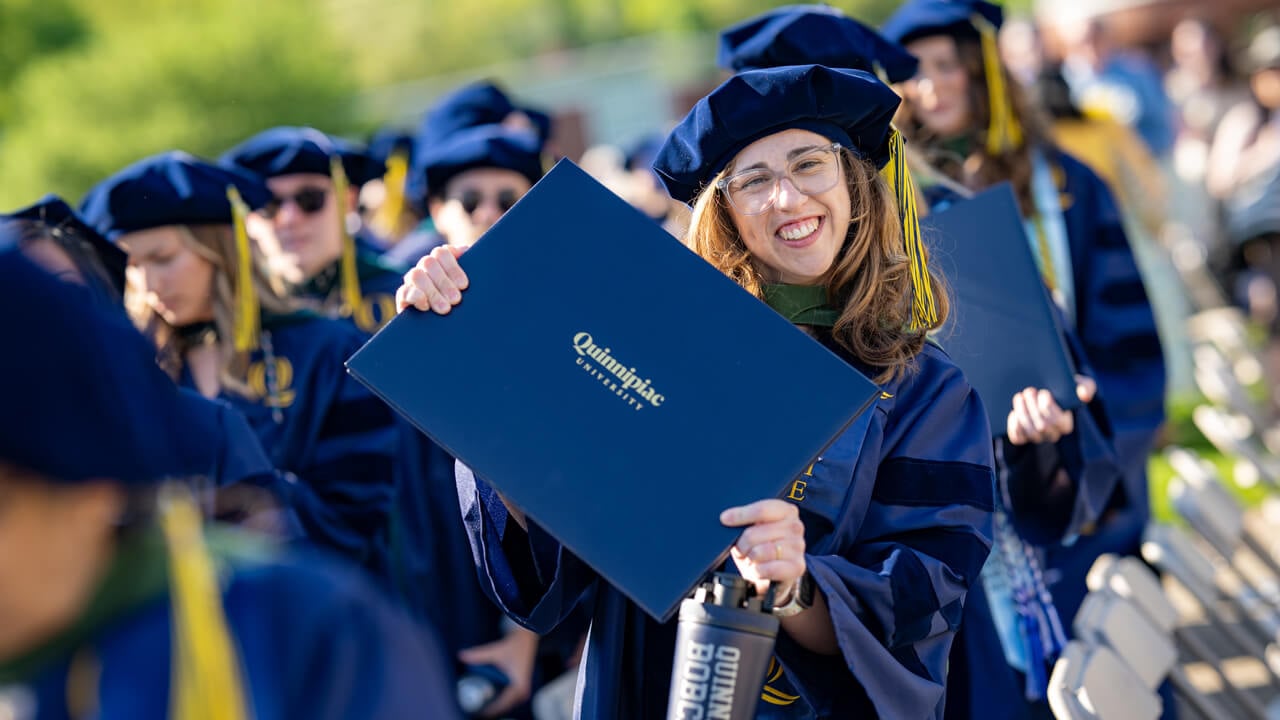 Graduate smiles holding out their diploma.