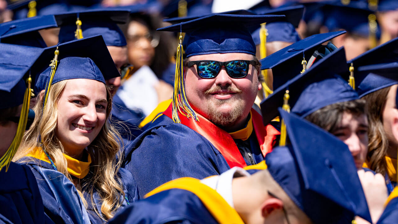 Graduates smile from their seats in the crowd.