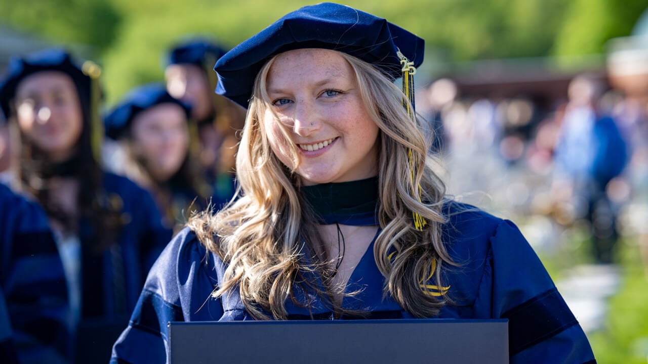 A graduate wearing a doctoral cap smiles at the camera