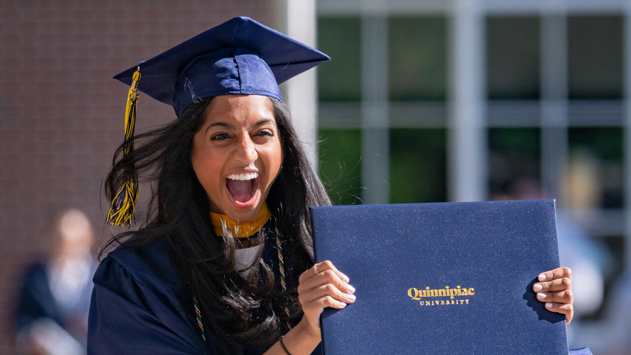 A grad excitedly holding up her diploma