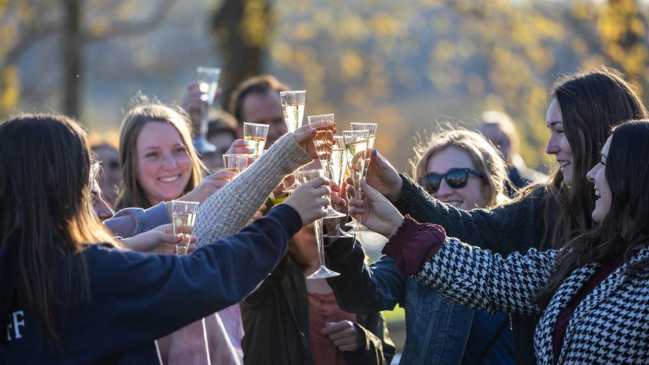 A dozen graduating students cheers with glasses of champagne