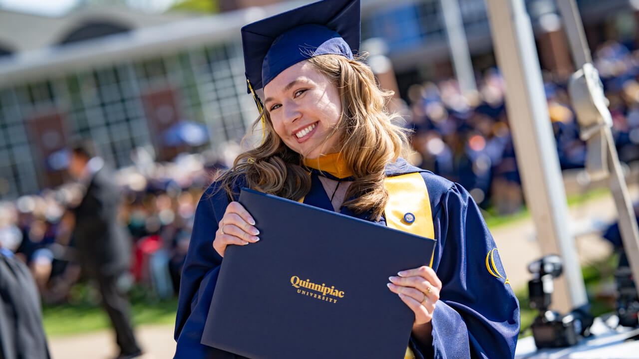 A grad smiling softly as they hold up their diploma