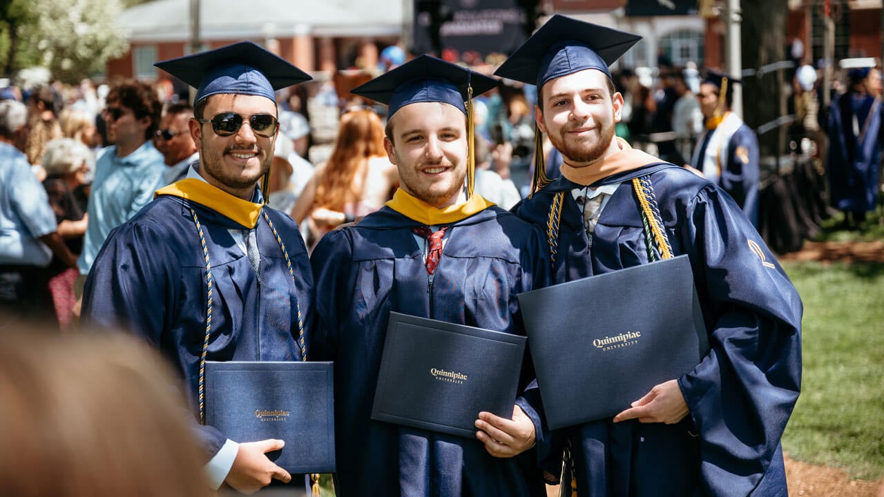 Three graduates smile and pose with their diplomas.