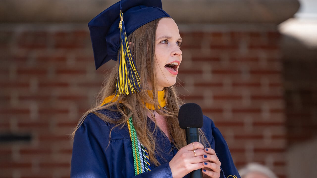 Gabrielle Sparks holds a microphone and sings onstage during Commencement