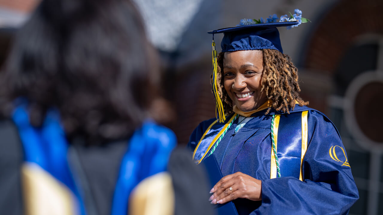 A grad holding their diploma and smiling