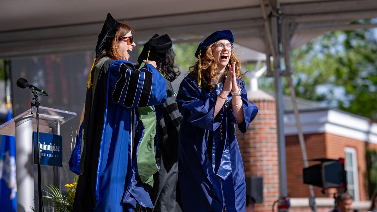 A grad clapping on stage as she gets hooded