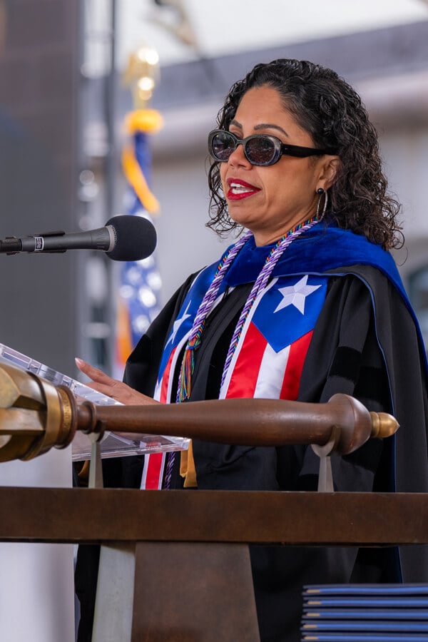 Tina Loarte-Rodriguez wears Commencement robes and a Puerto Rico stole and speaks at a podium