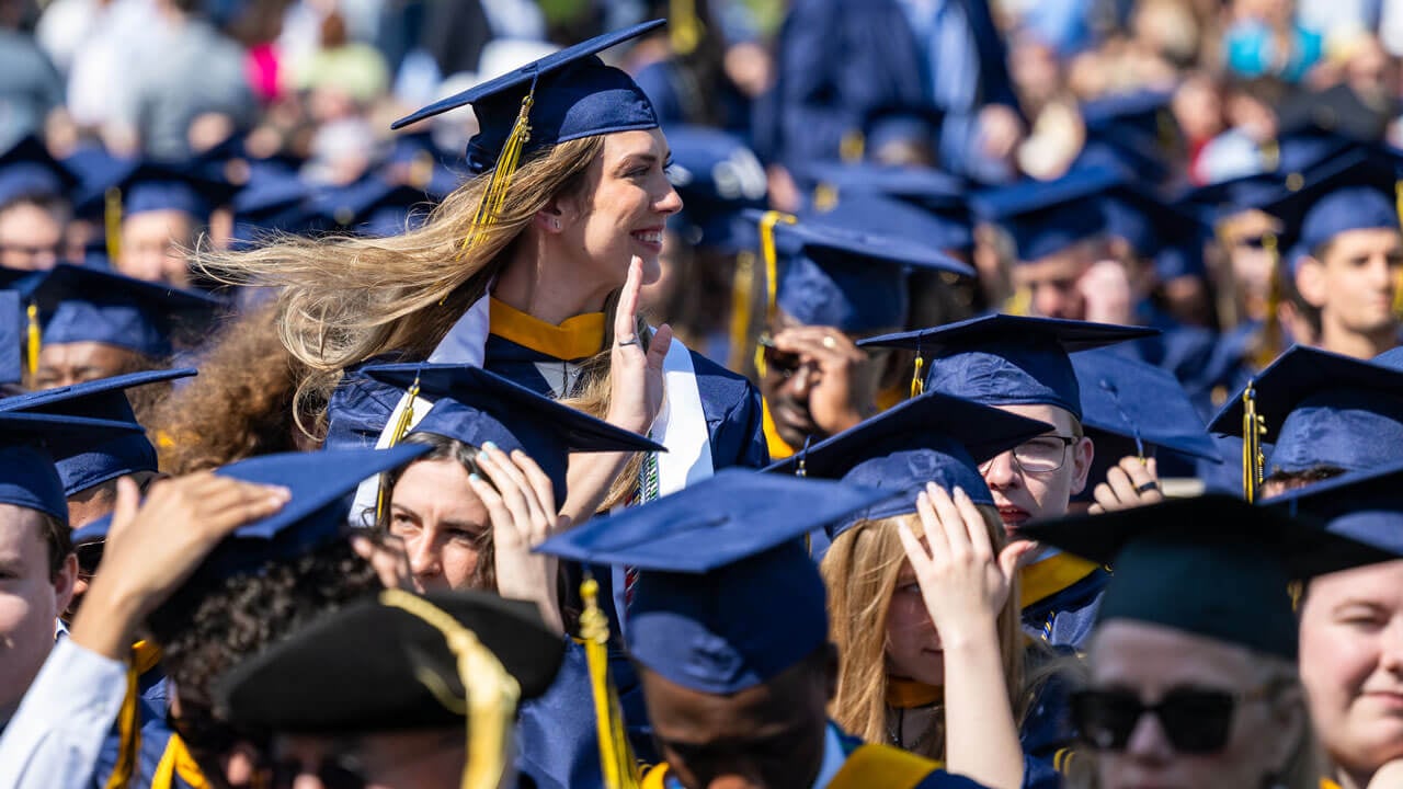 Graduate stands and waves in the crowd.
