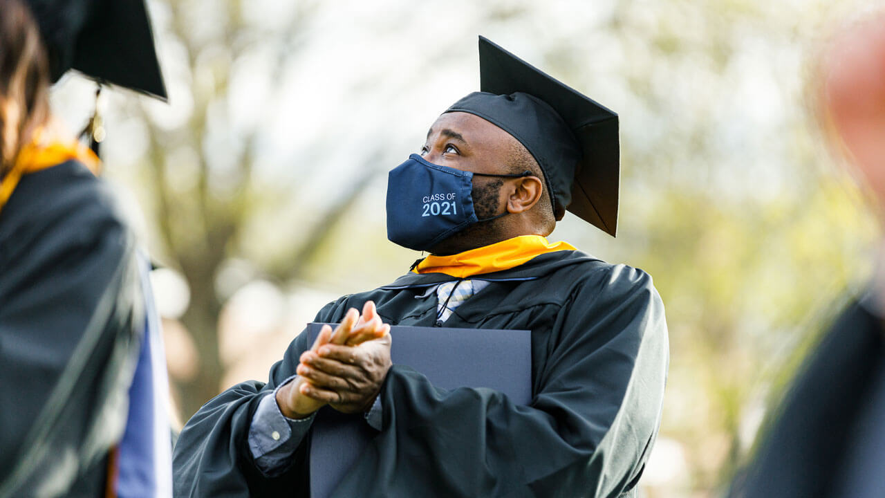 A graduate looks up and claps during Commencement