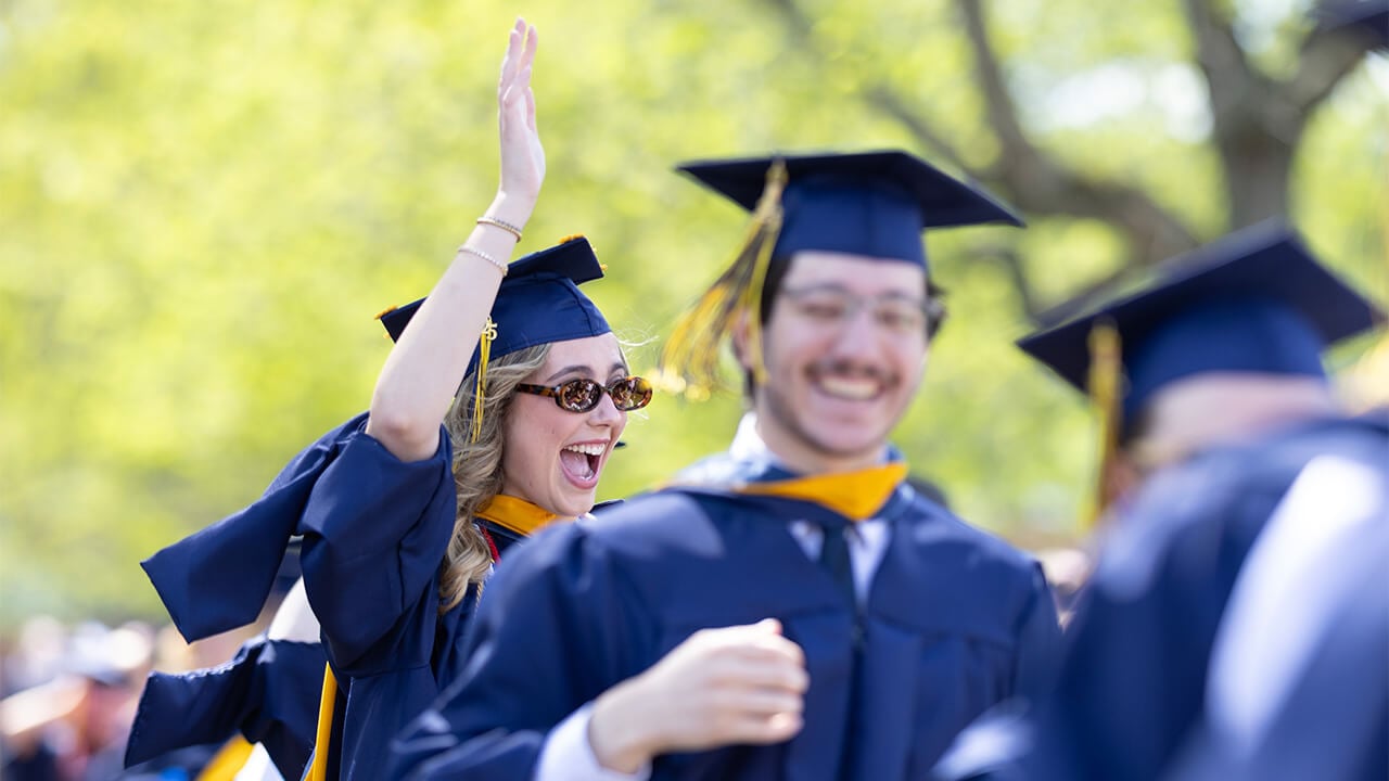 Student waves in cap and gown.