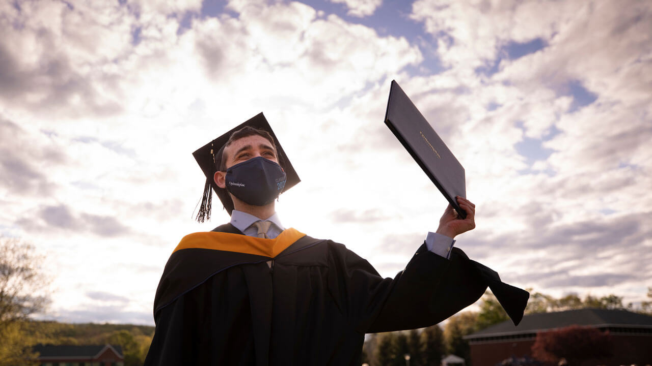The sun shines over the shoulder of a graduate as he celebrates