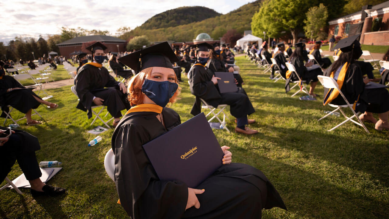 Graduates proudly hold up their diploma covers as the sun casts long shadows