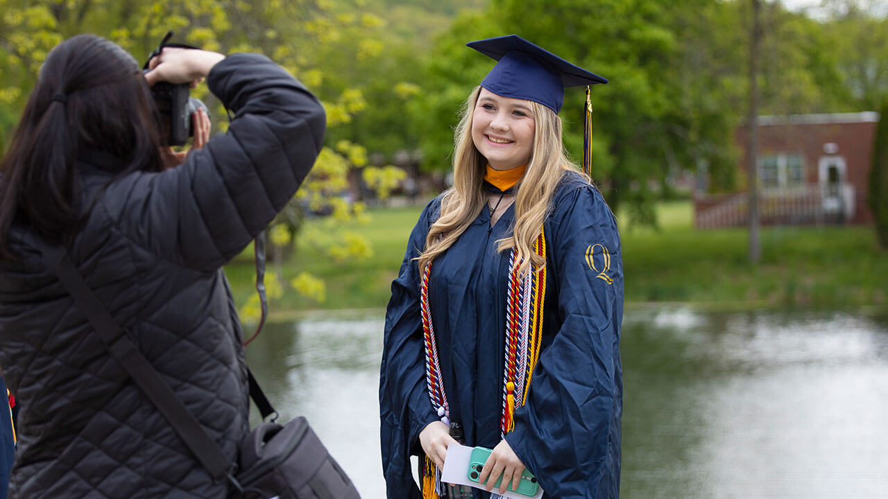 A graduate poses for a photo with her family member in front of a pond adjacent to the quad