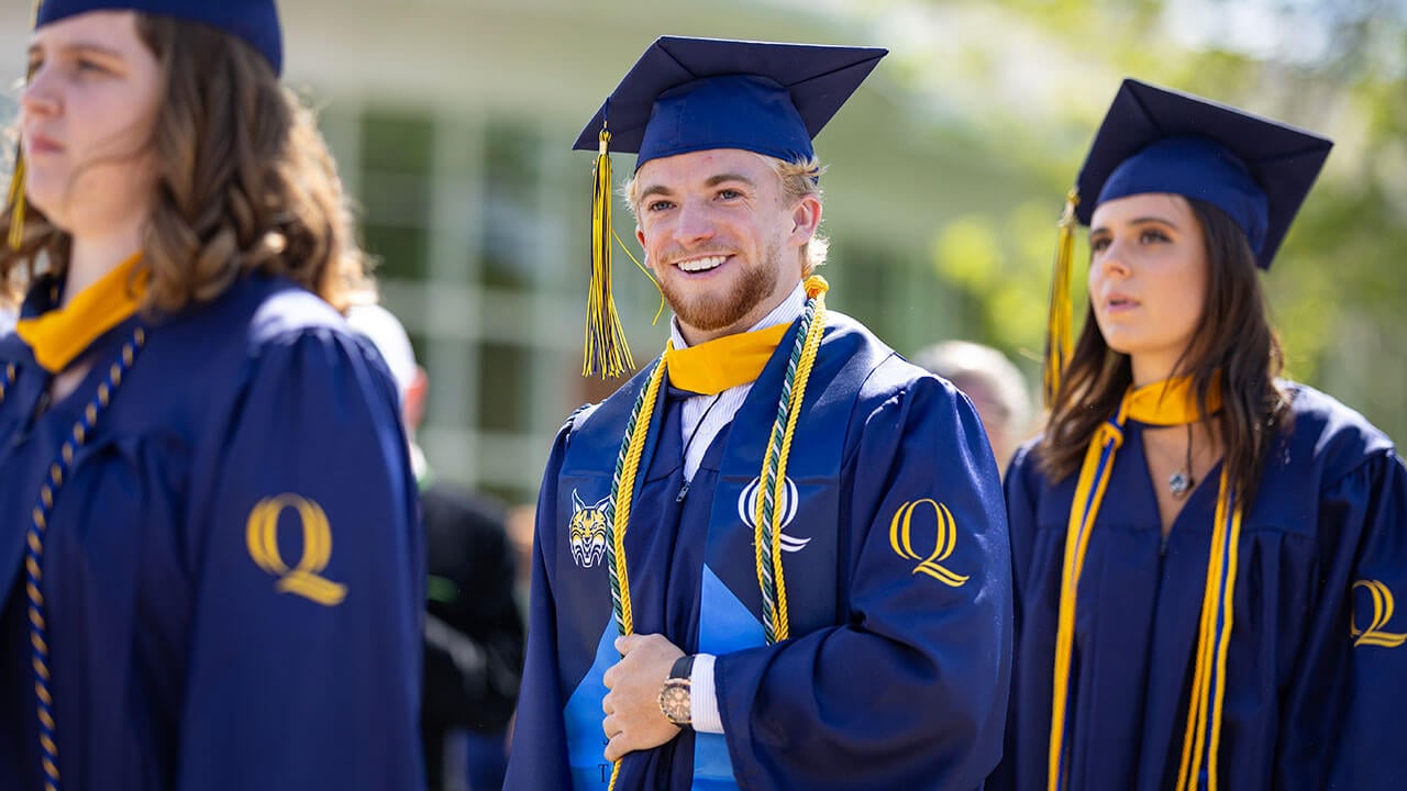 A Quinnipiac student athlete smiles as he processes in