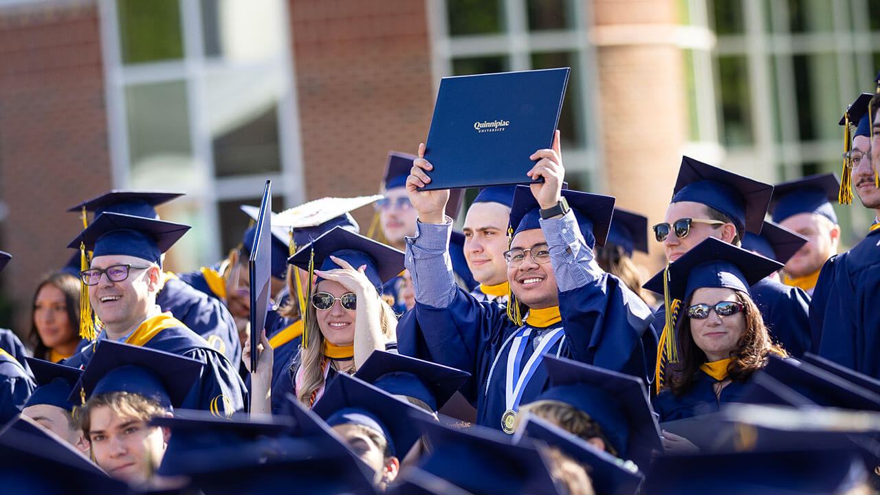 A graduate holds up their diploma and cheers