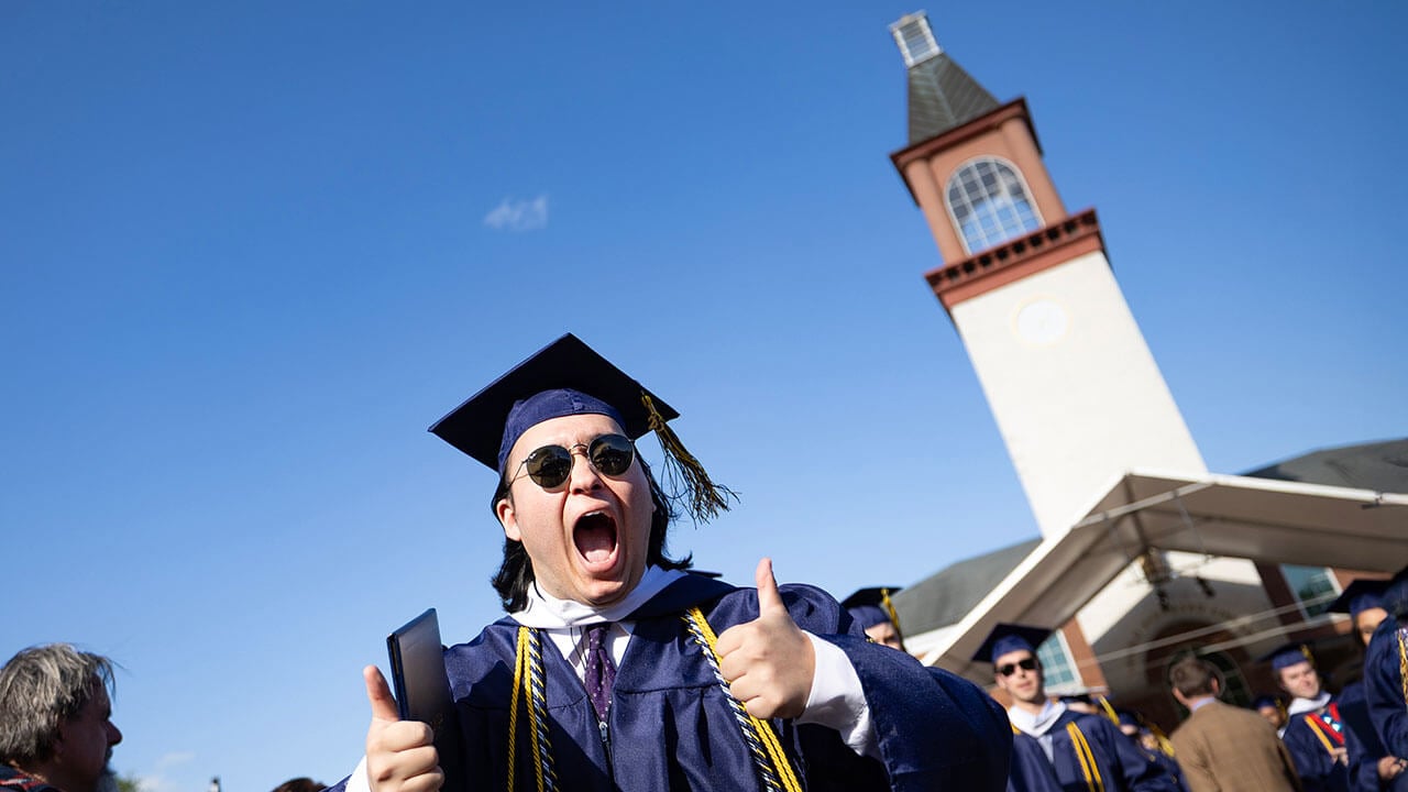 A graduate cheers as he walks in front of the Arnold Bernhard Library