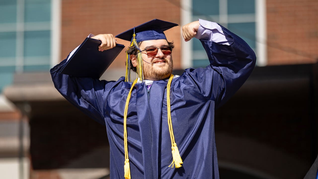 Graduate poses with their arms up after accepting their diploma.