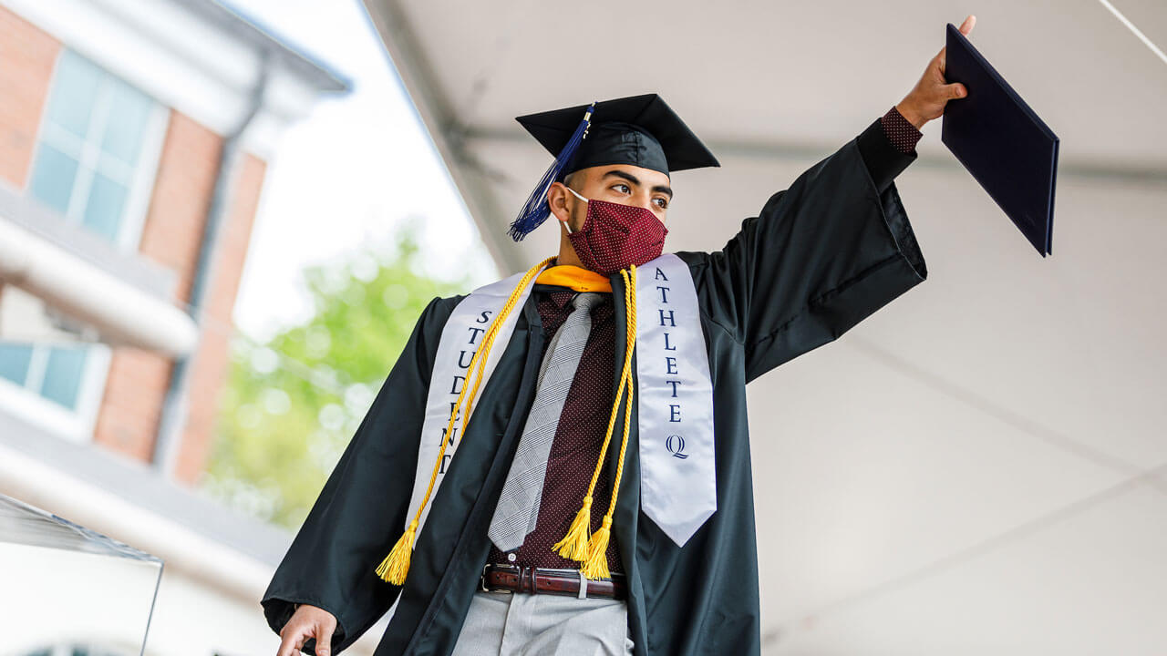A student holds up his diploma cover as he walks across the stage