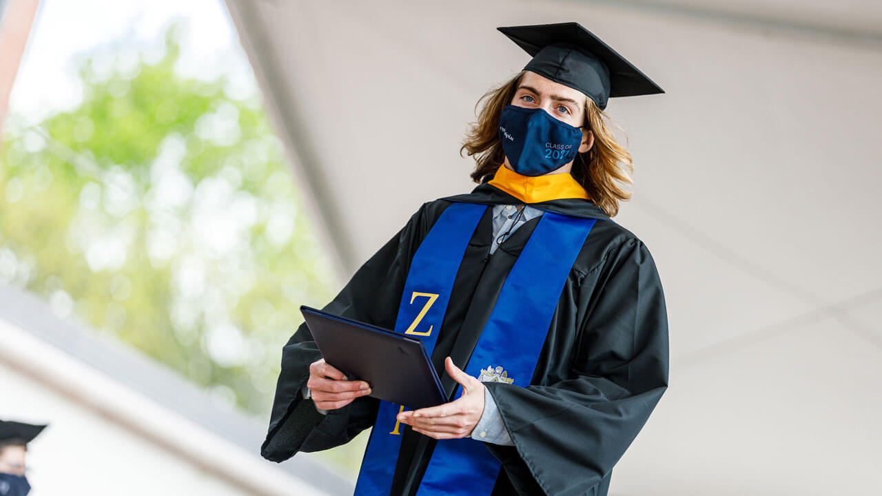 A graduate carries his diploma cover across the Commencement stage