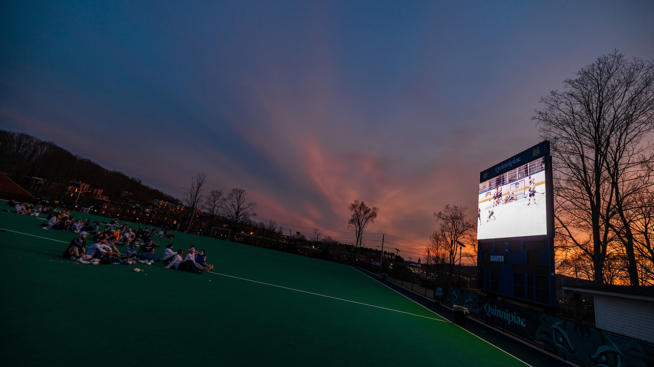 Students watch hockey on the field hockey field.