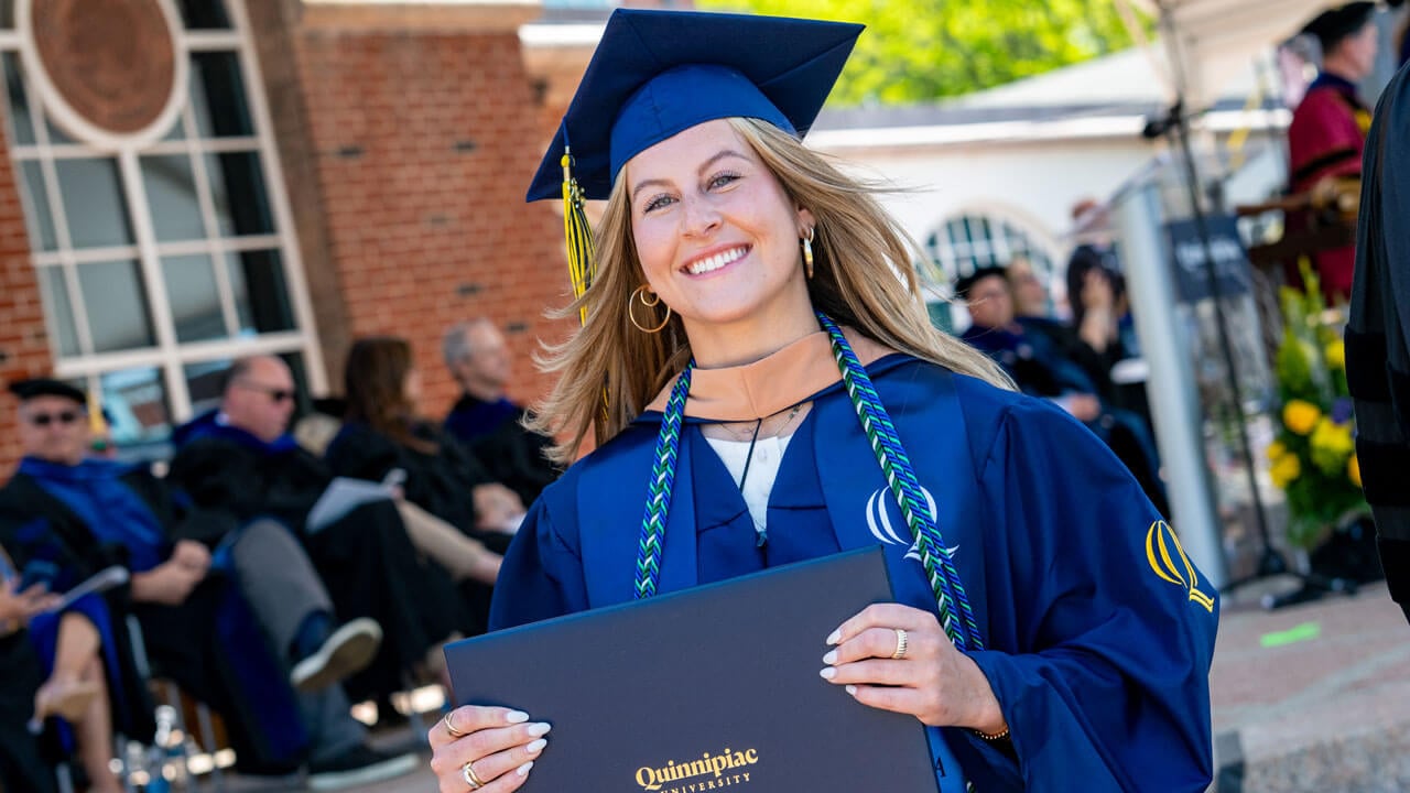 Graduate smiles with their diploma as the exit the commencement stage.