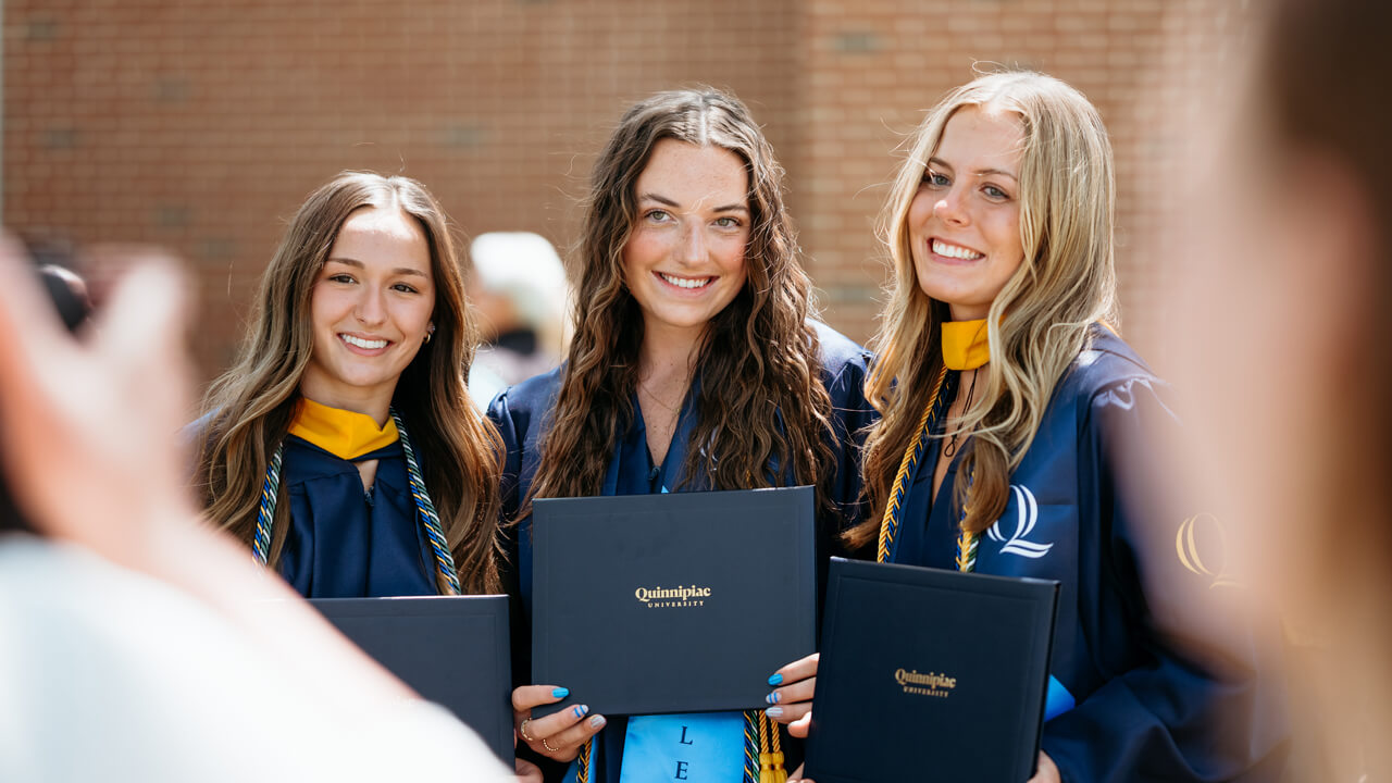 Three graduates pose and smile with their diplomas.
