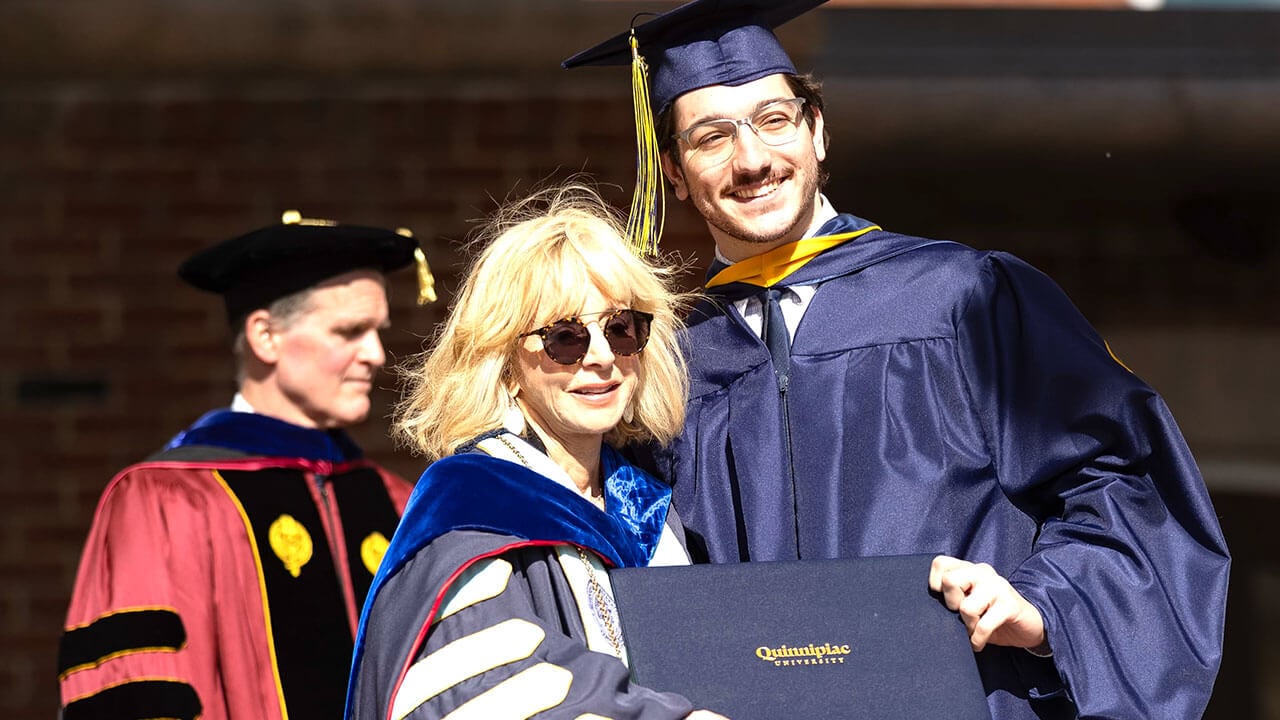 President Judy Olian and a student smiling on stage with diploma