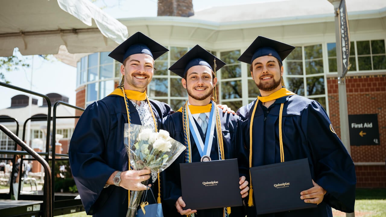 Three male graduates smile together for a group photo.