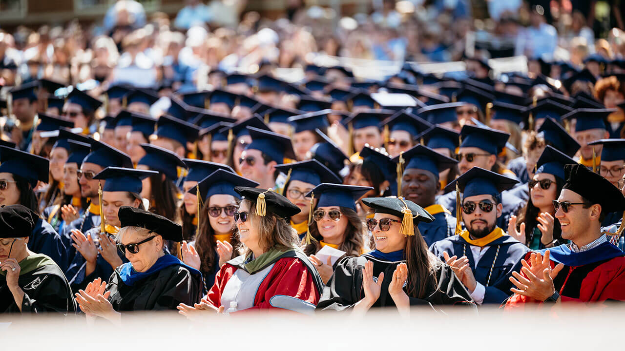 A crowd of graduates and faculty sitting in chairs on the quad