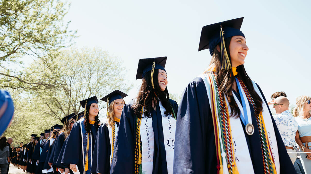 4 graduates processing in and smiling towards the library